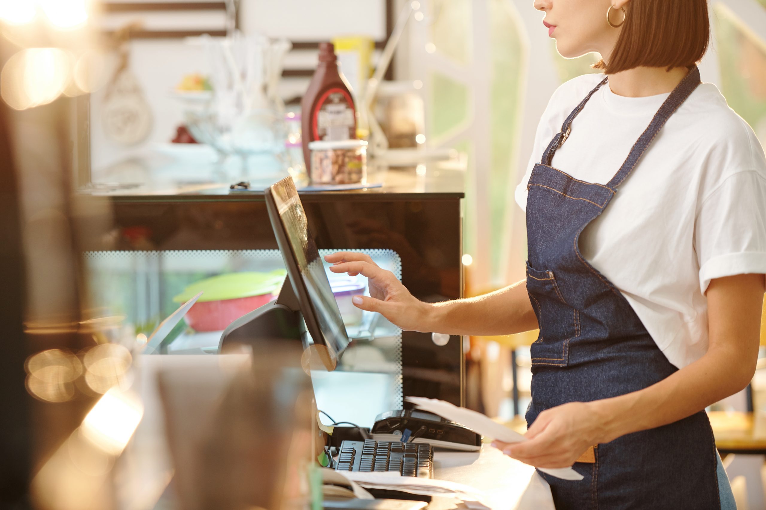 Cropped image of female barista working at coffeeshop and using cash register when accepting payment or entering order detaikls